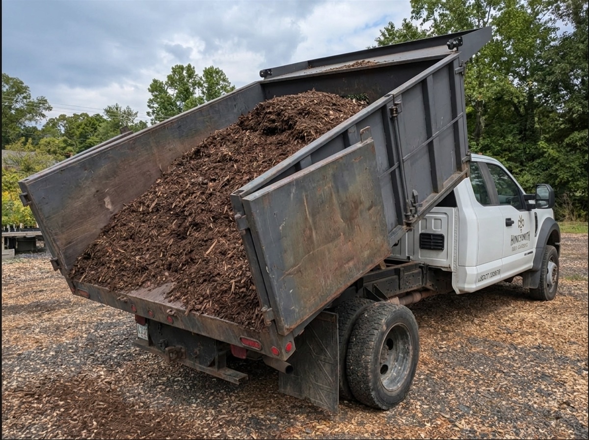 Honeysmith dump truck with its bed raised, unloading a full load of bulk mulch on the lot